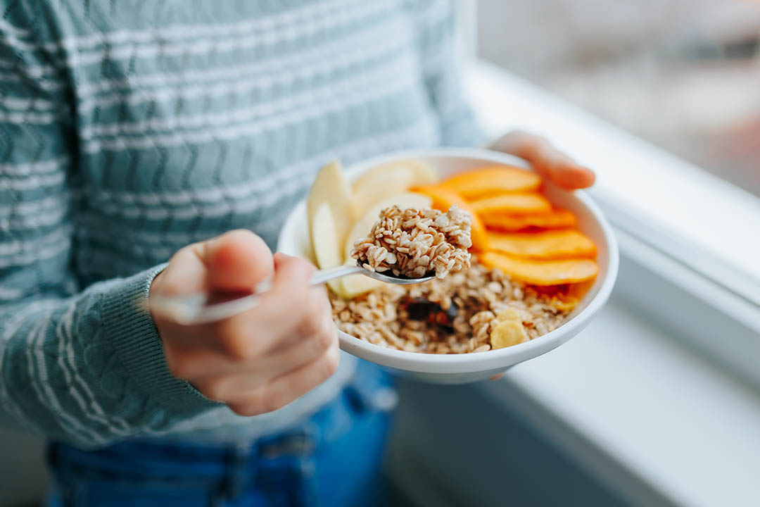 Young woman with muesli bowl, girl eating breakfast cereals nuts, pumpkin, oats and apple in bowl.