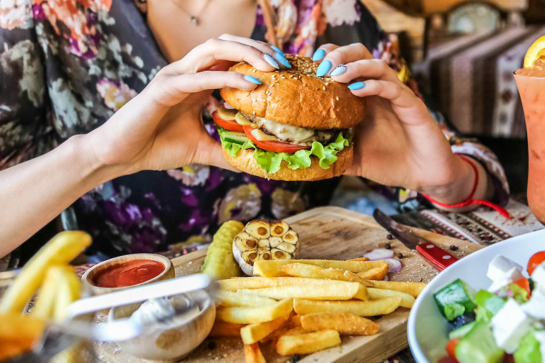 Kidney Stones - side view woman eating meat burger with fries ketchup and mayonnaise on a wooden stand